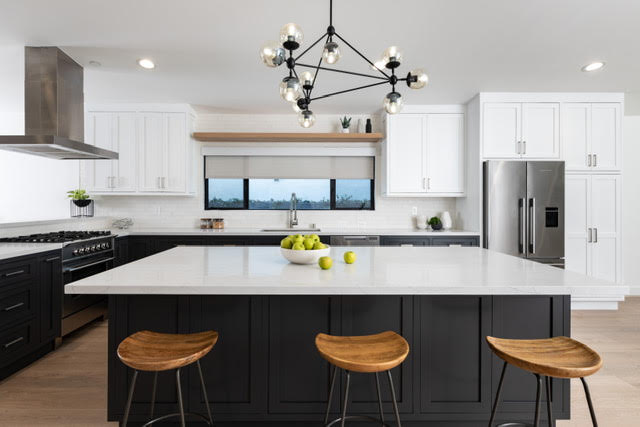 Two-tone kitchen with white shaker cabinets, black island base, oversized white island, geometric chandelier, and stainless refrigerator.