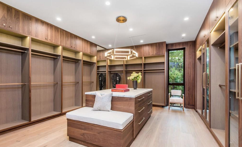 Walk-in closet with walnut built-ins, marble-topped island, and geometric pendant lighting.