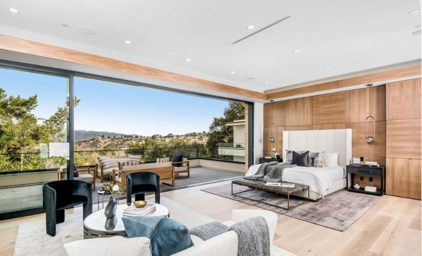 Modern bedroom with wood accent wall, large sliding glass doors, and terrace seating with hillside view.
